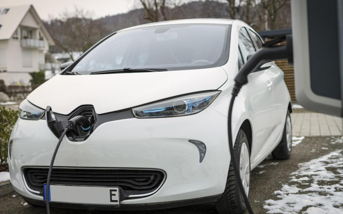 Beli električni automobil se puni na kućnom punjaču u dvorištu