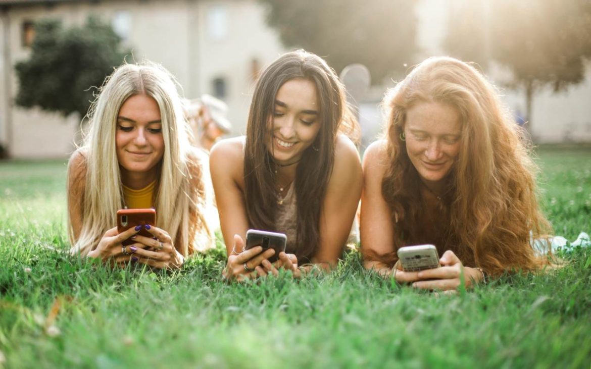 Tri devojke leže na travi i gledaju u telefone