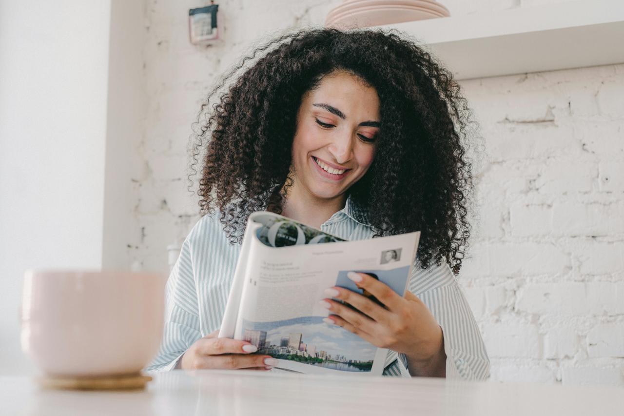 Žena sa kovrdžavom kosom čita časopis i smeši se