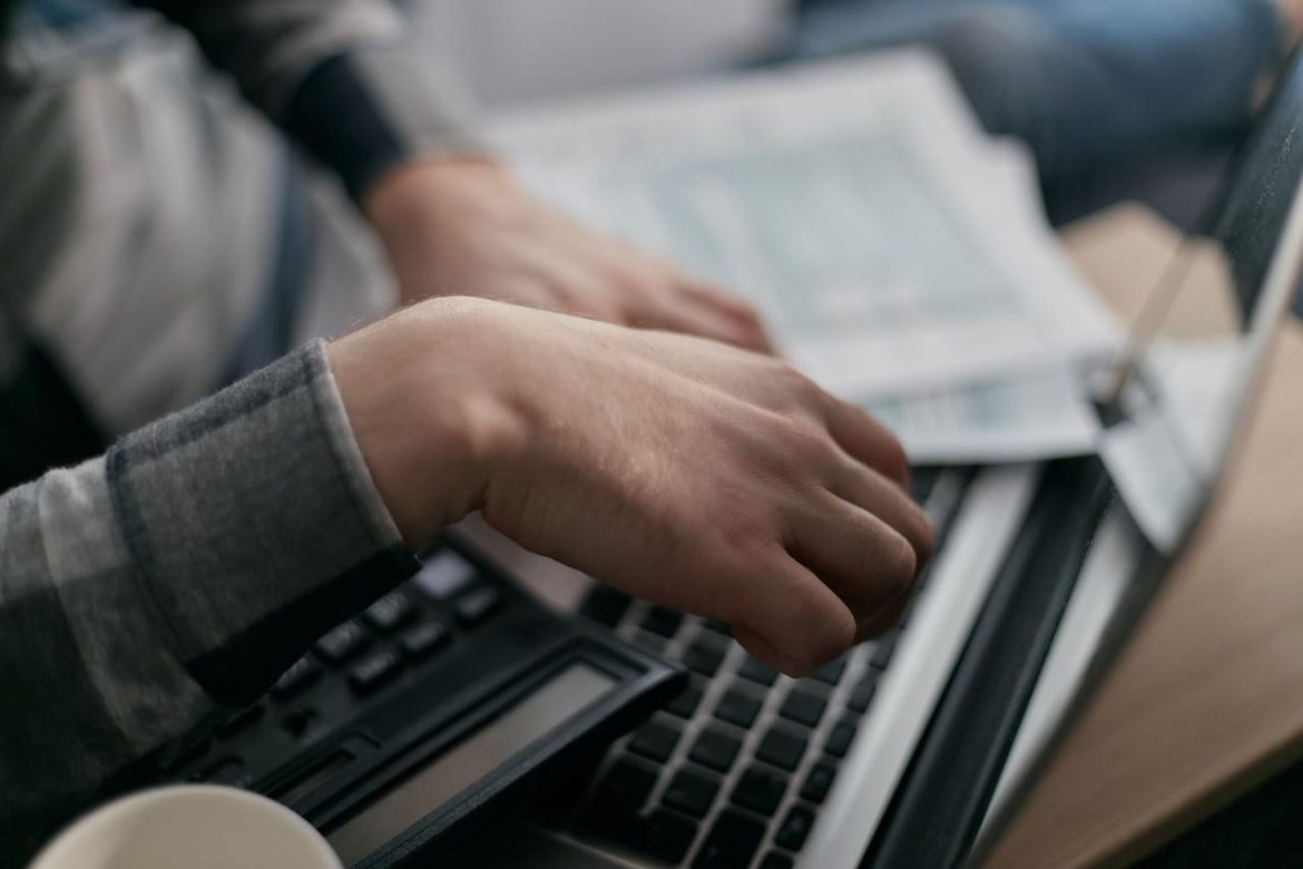 Ruke koje kucaju na tastaturi računara pored dokumenata